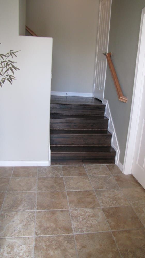 Stairs with dark wood treads and risers leading up from a tile-floored entryway with light gray walls.