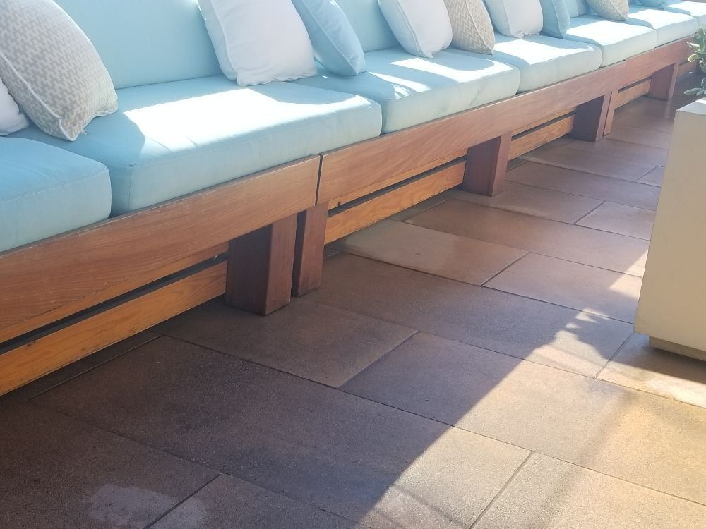 Long wooden bench seat with light blue cushions and white pillows on a stone patio.