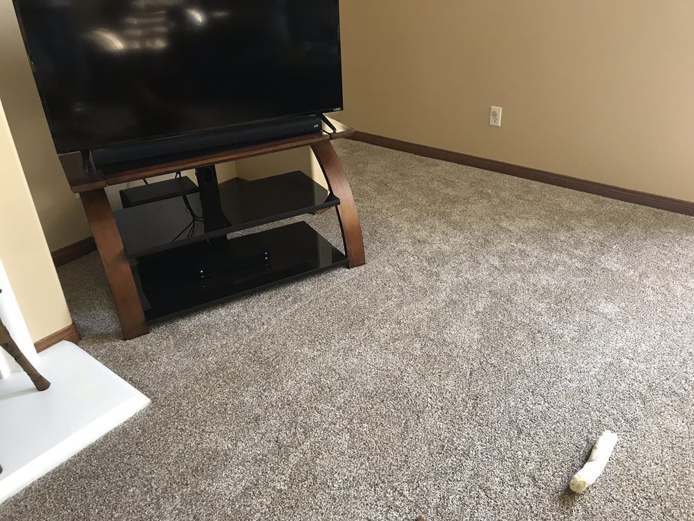 A television on a black glass and wood stand sits on beige carpet in a room with tan walls and a white base.