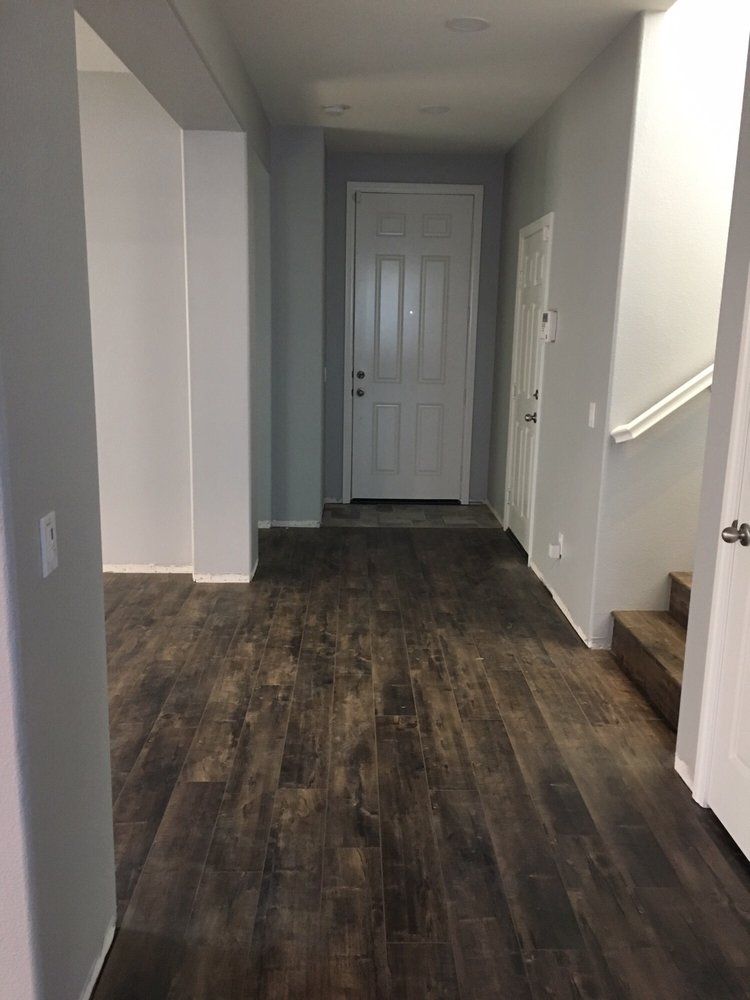 A bright entryway with dark wood-look floors, grey walls, a white front door, and a staircase on the right.