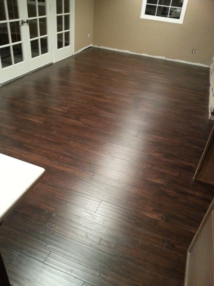 Dark wood laminate flooring stretches across an empty room featuring white French doors and beige walls.