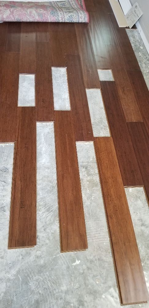 Brown wood floor planks installed in a staggered pattern over a gray concrete subfloor.