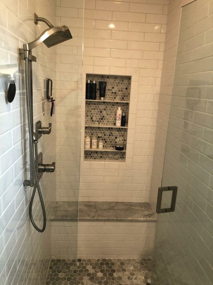 A modern shower with white subway tile walls, a marble bench, and a recessed shelf featuring pebble-style tiling.