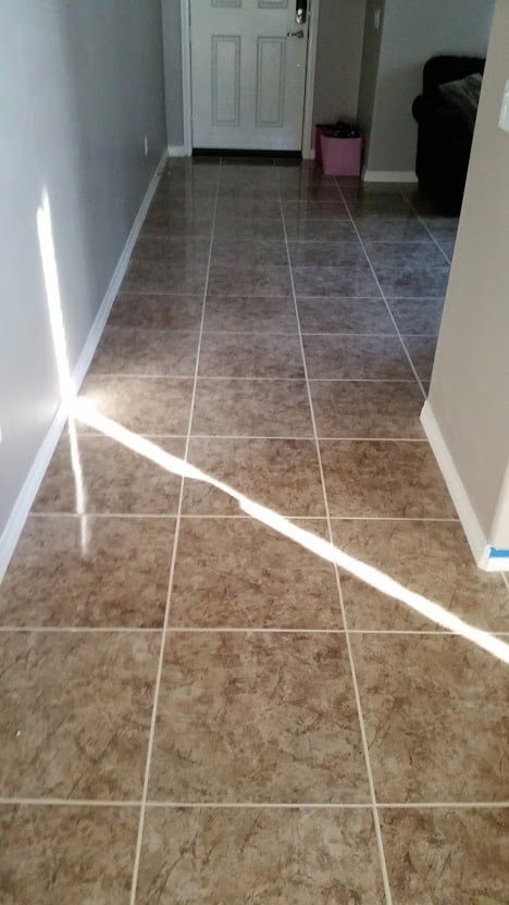 A hallway with brown, stone-look tile flooring and a bright beam of sunlight casting a diagonal line across the floor.