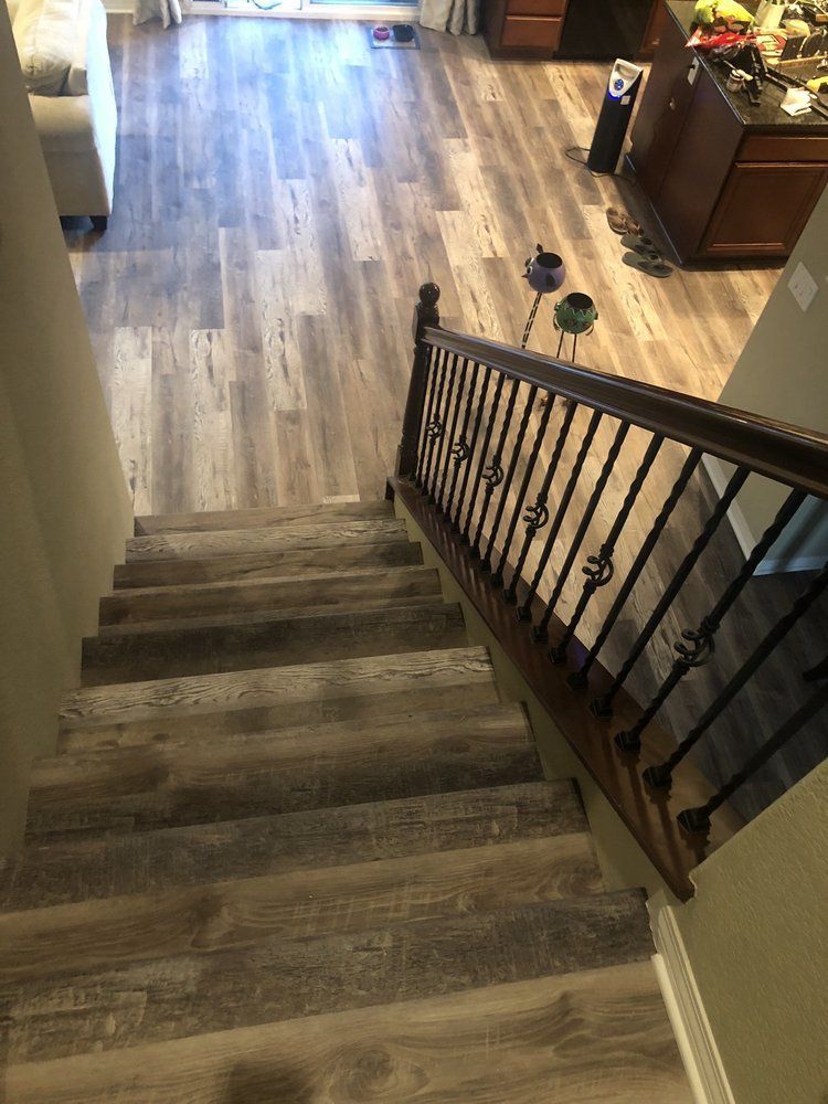 A downward view of stairs with gray wood-look flooring leading to an open living area with matching floors.
