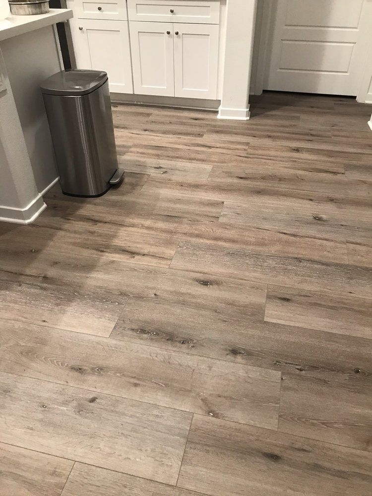 Light wood-look plank flooring in a kitchen near a stainless steel trash can and white cabinetry.