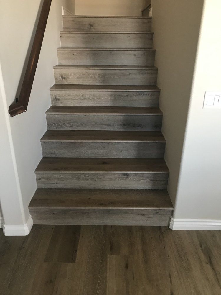 Straight wooden staircase with gray, wood-grain planks leading upward between two plain walls.