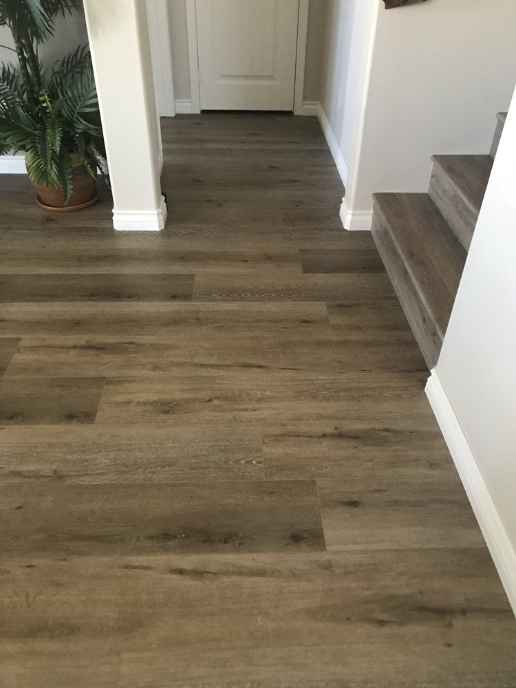 An indoor hallway featuring wood-grain laminate flooring, a white baseboard, a staircase, and a potted plant.