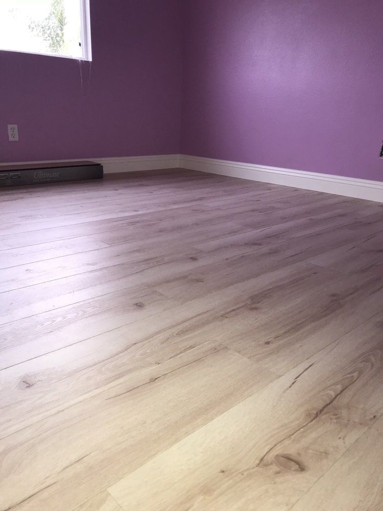 A room with light-toned wood flooring and purple walls featuring white baseboards and a window.