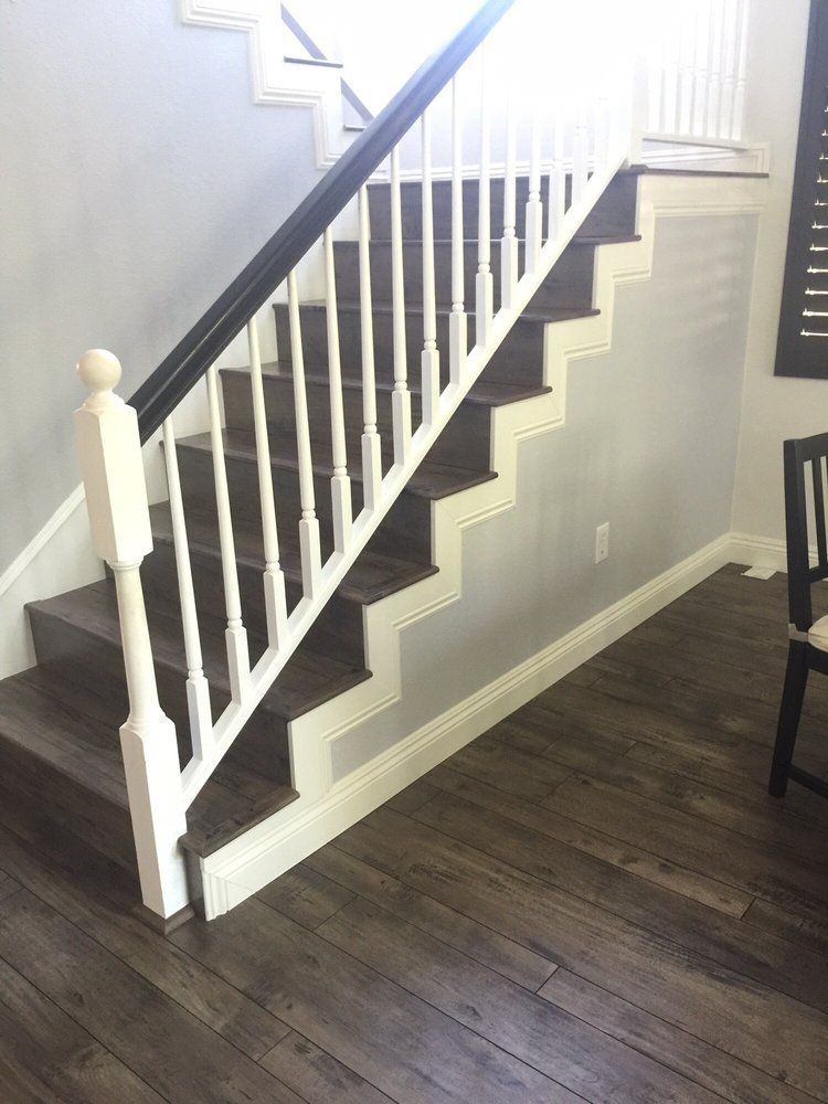 A staircase with dark wood treads and a white railing, set against a light gray wall with dark hardwood flooring.