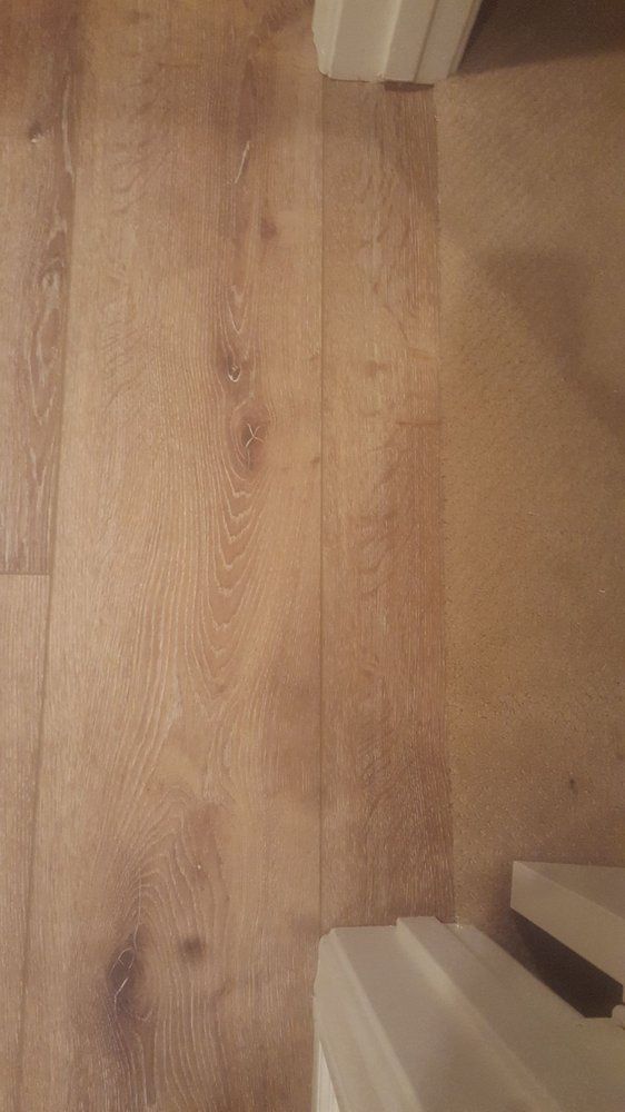 A top-down view showing a transition between light wood-grain flooring and tan carpet, divided by a doorway threshold.