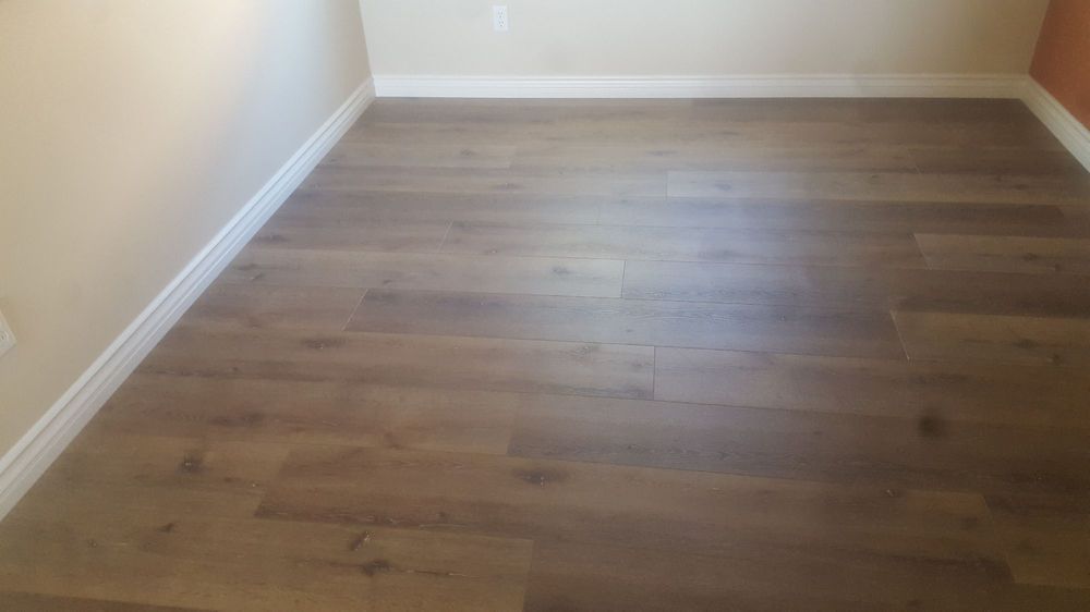 Empty room with light beige walls, white baseboards, and brown wood-look plank flooring.