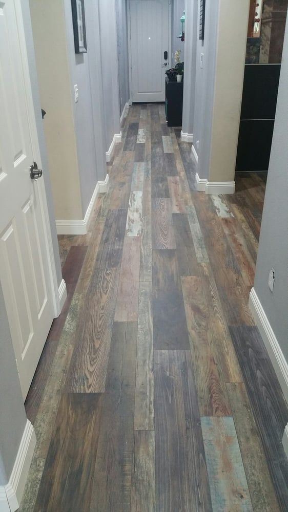 A hallway featuring wood-look vinyl plank flooring with a varied, multi-toned pattern, grey walls, and white trim.