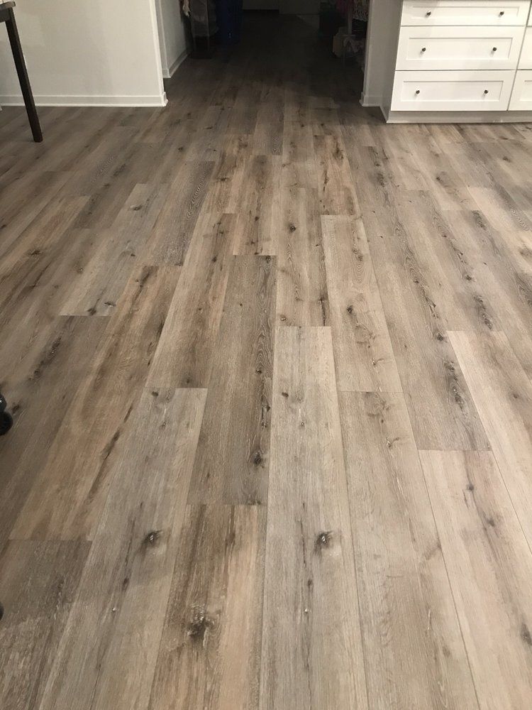 Light gray wood-look luxury vinyl plank flooring installed in a residential room with white cabinetry in the background.