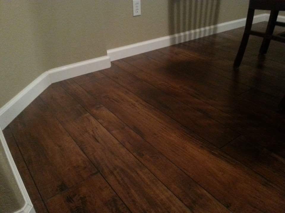 Dark wood flooring with white baseboards in an interior room corner.