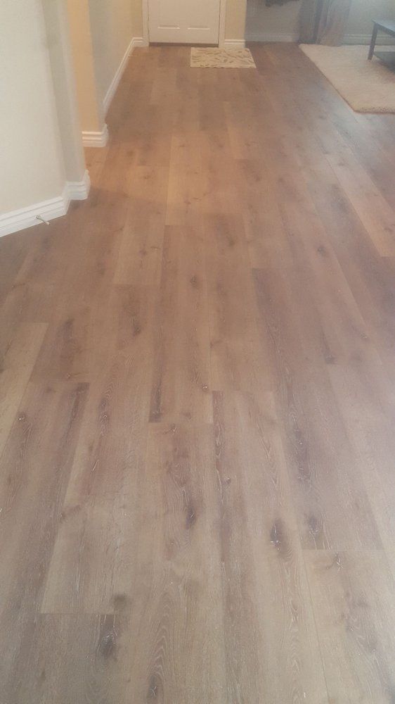 A hallway with light brown wood-look flooring leading toward a closed white door.