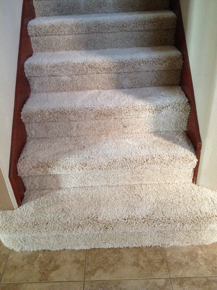 A staircase with five carpeted steps leading upward, bordered by wooden trim, transitioning to tiled flooring at the base.