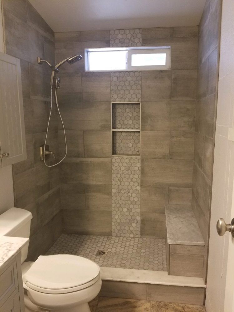 A walk-in shower with brown wood-look tiles, a pebble-tile niche and floor, a built-in bench, and a handheld sprayer.