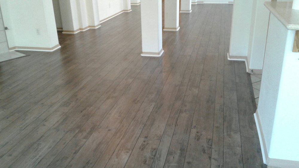 Wide-angle shot of a room with light-brown, wood-grain plank flooring, white pillars, and beige walls.