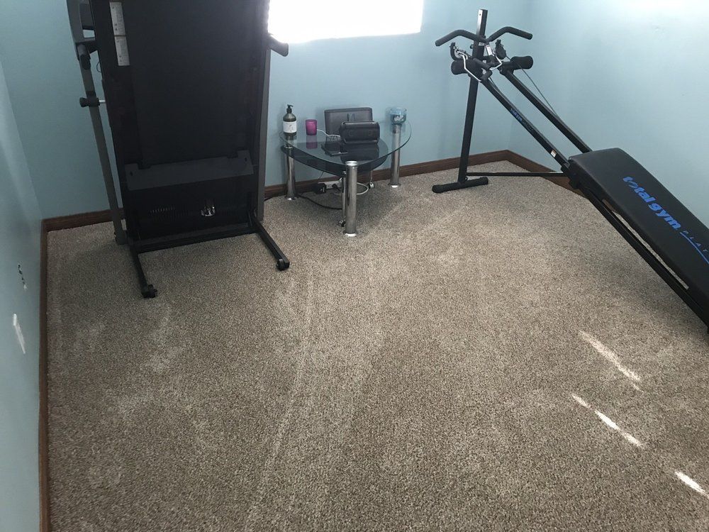 A home workout space with a folded treadmill, a small glass side table, and a Total Gym exercise machine on beige carpet.