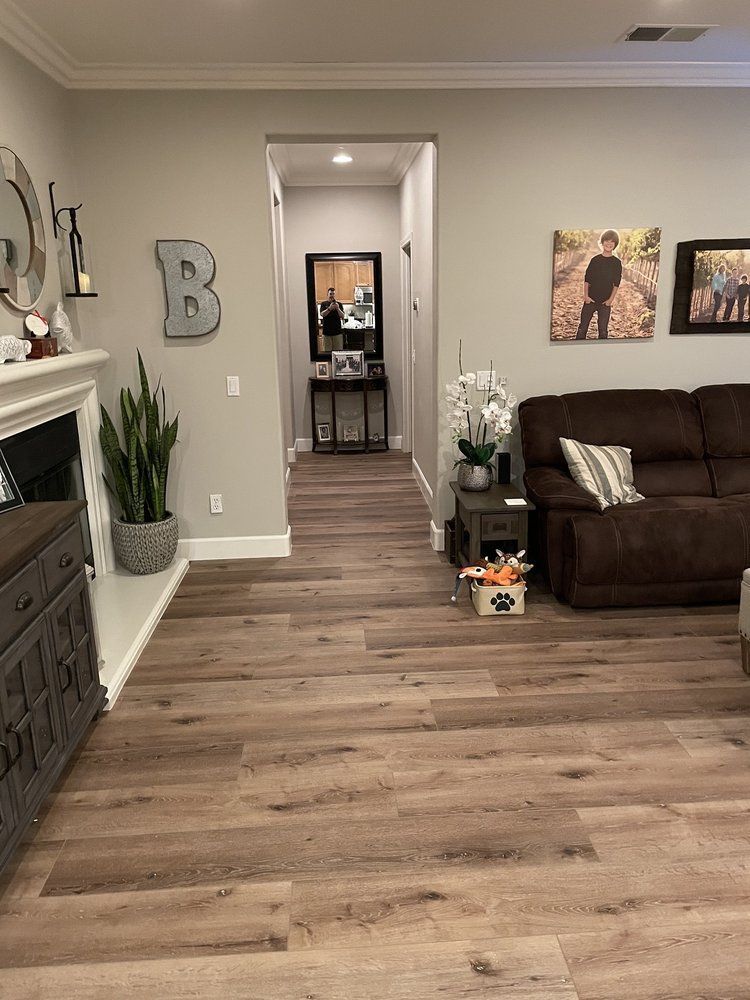 A living room with light wood-look flooring, a fireplace, a brown sofa, and a hallway leading to a mirror and console table.