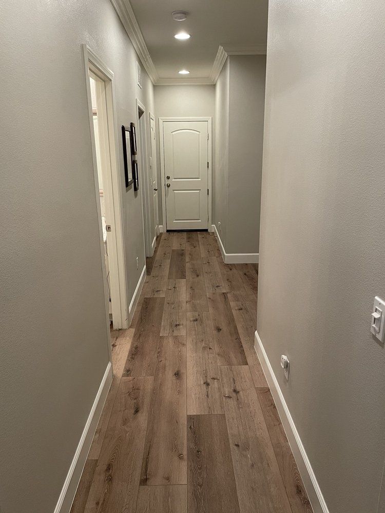 A hallway with light gray walls, wood-look flooring, and recessed ceiling lighting, leading to a closed white door.