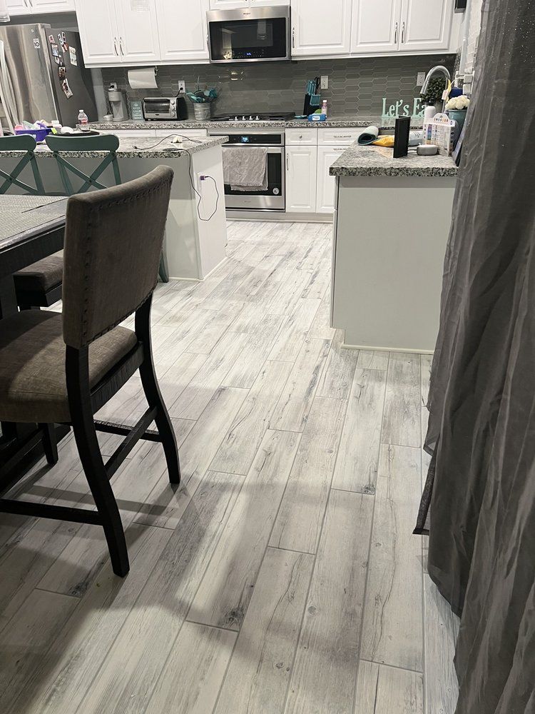 A kitchen view featuring light grey wood-look flooring, white cabinets, stainless steel appliances, and a dining chair.