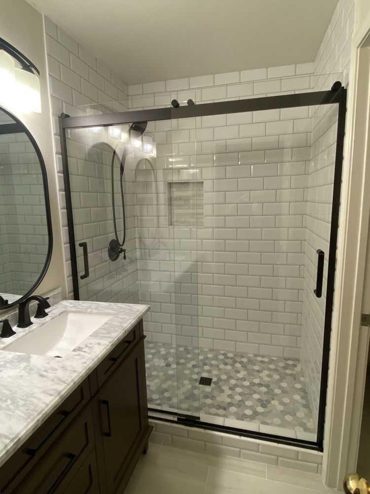 A bathroom featuring a vanity with a white marble countertop next to a glass-enclosed shower with white subway tile.