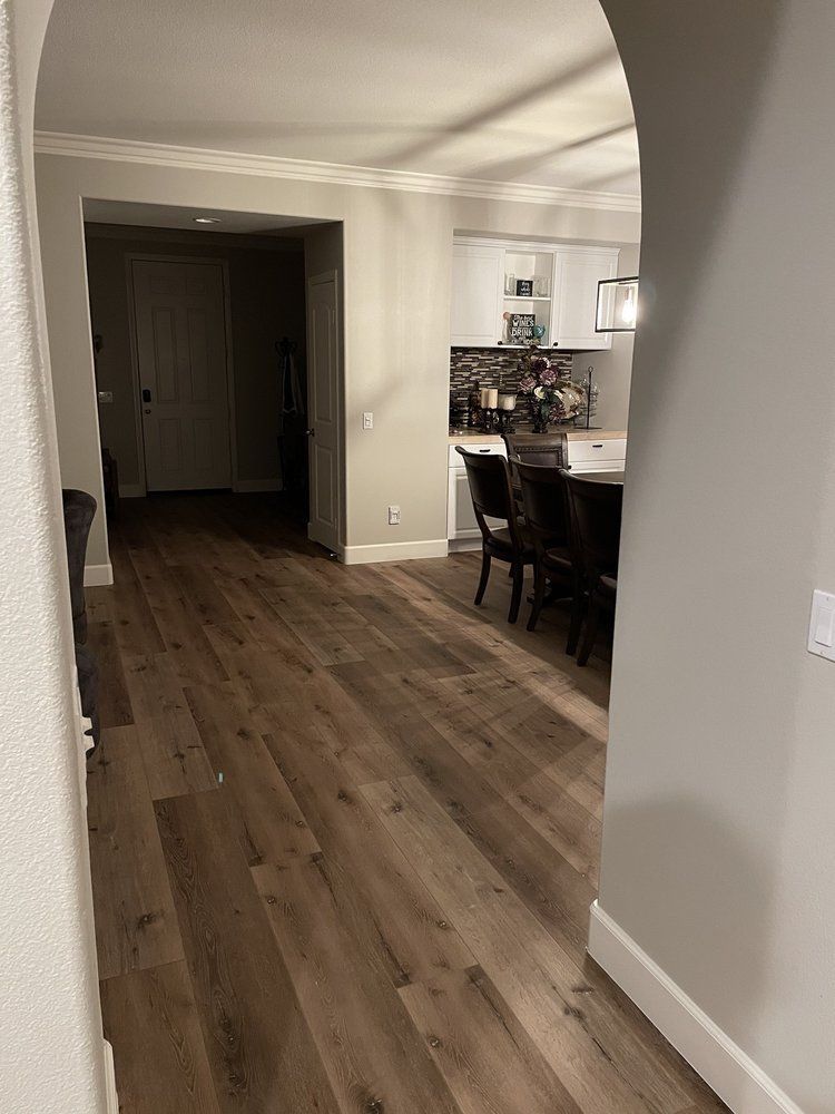 A view from an arched doorway looking across wood flooring into a brightly lit dining area with dark chairs and table.