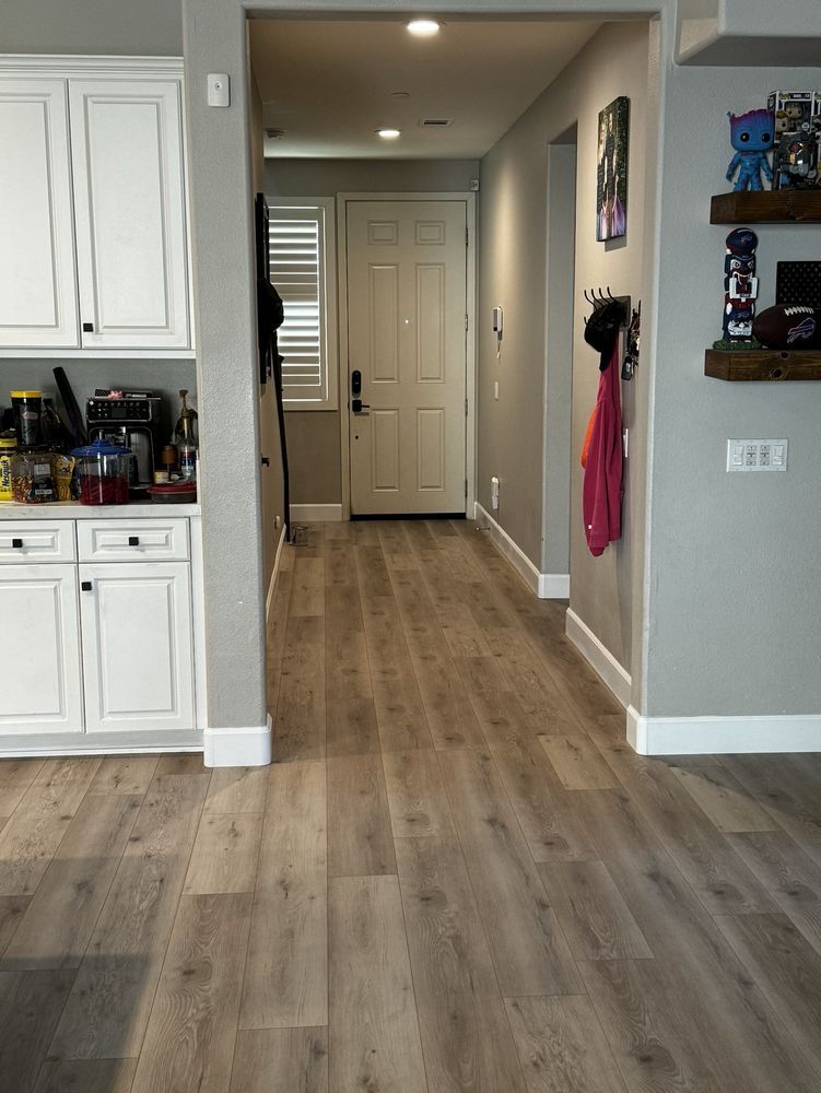 A view from a kitchen looking down a hallway toward a white front door, with light wood flooring and grey walls.