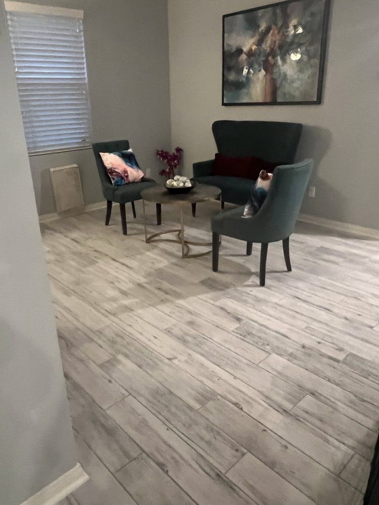 A seating area with light wood-look flooring, two blue armchairs, a dark gray sofa, a small coffee table, and wall art.