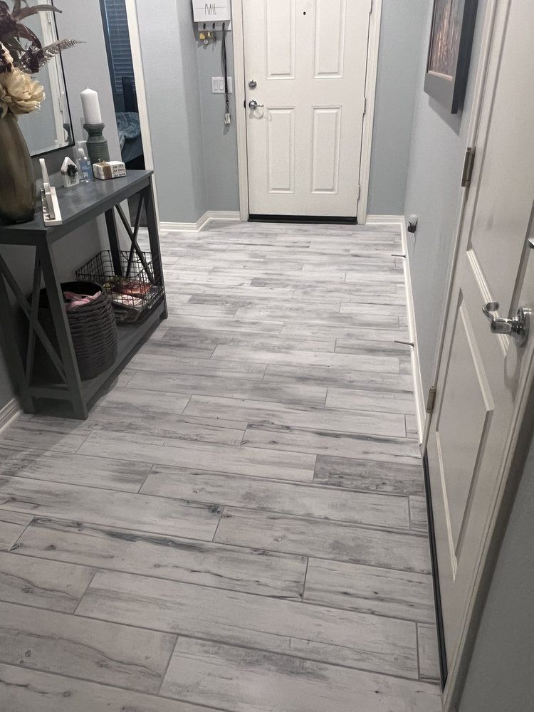 An entryway with gray wood-look plank flooring, a console table on the left, and a white front door in the background.