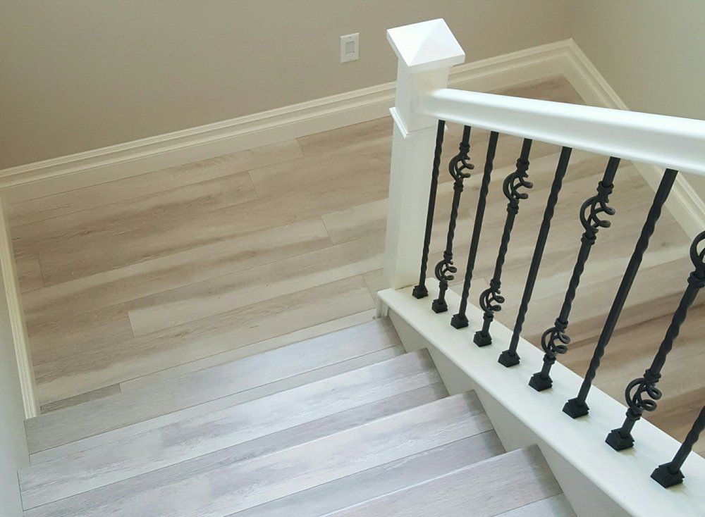 A high-angle view of a staircase with light wood steps, white railing, and decorative black metal balusters.