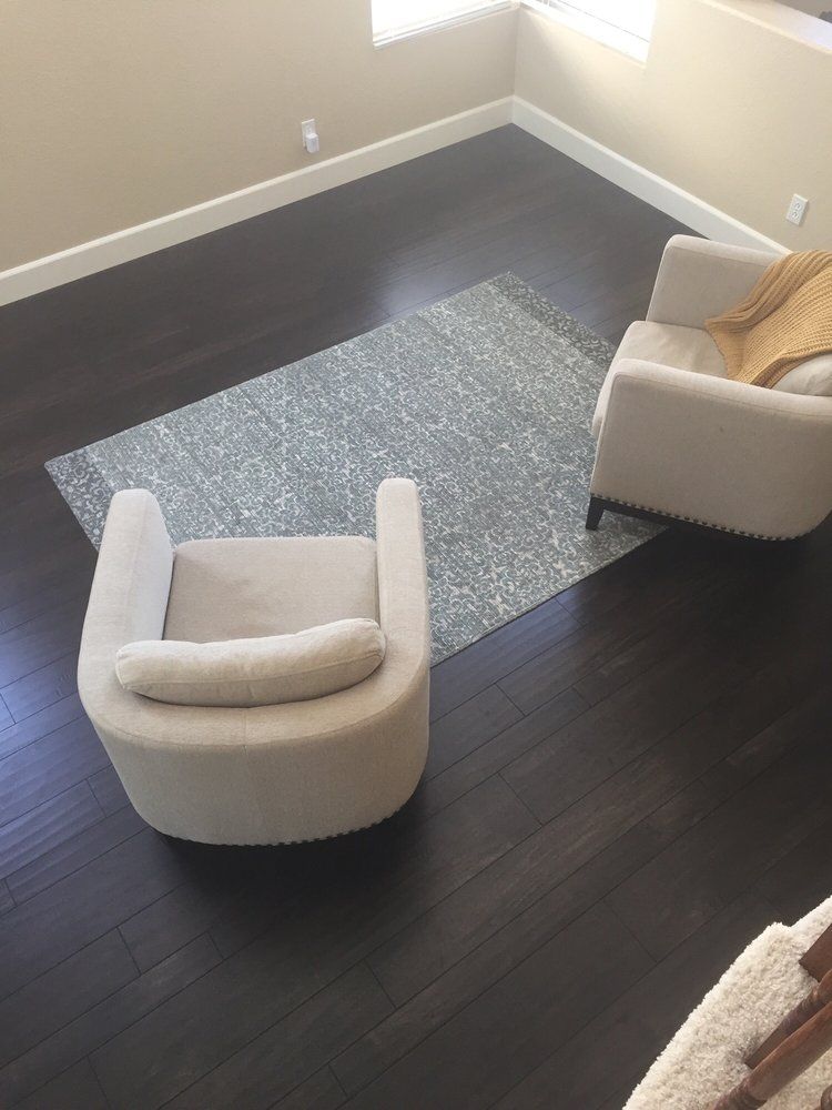Two beige armchairs facing each other on a gray patterned rug atop dark wood flooring in a brightly lit room.