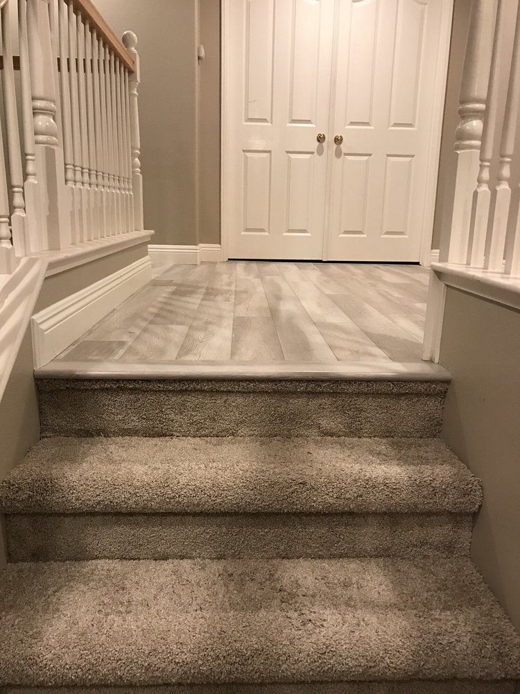 Two carpeted stairs leading up to a landing with light grey wood-look flooring and white double doors.
