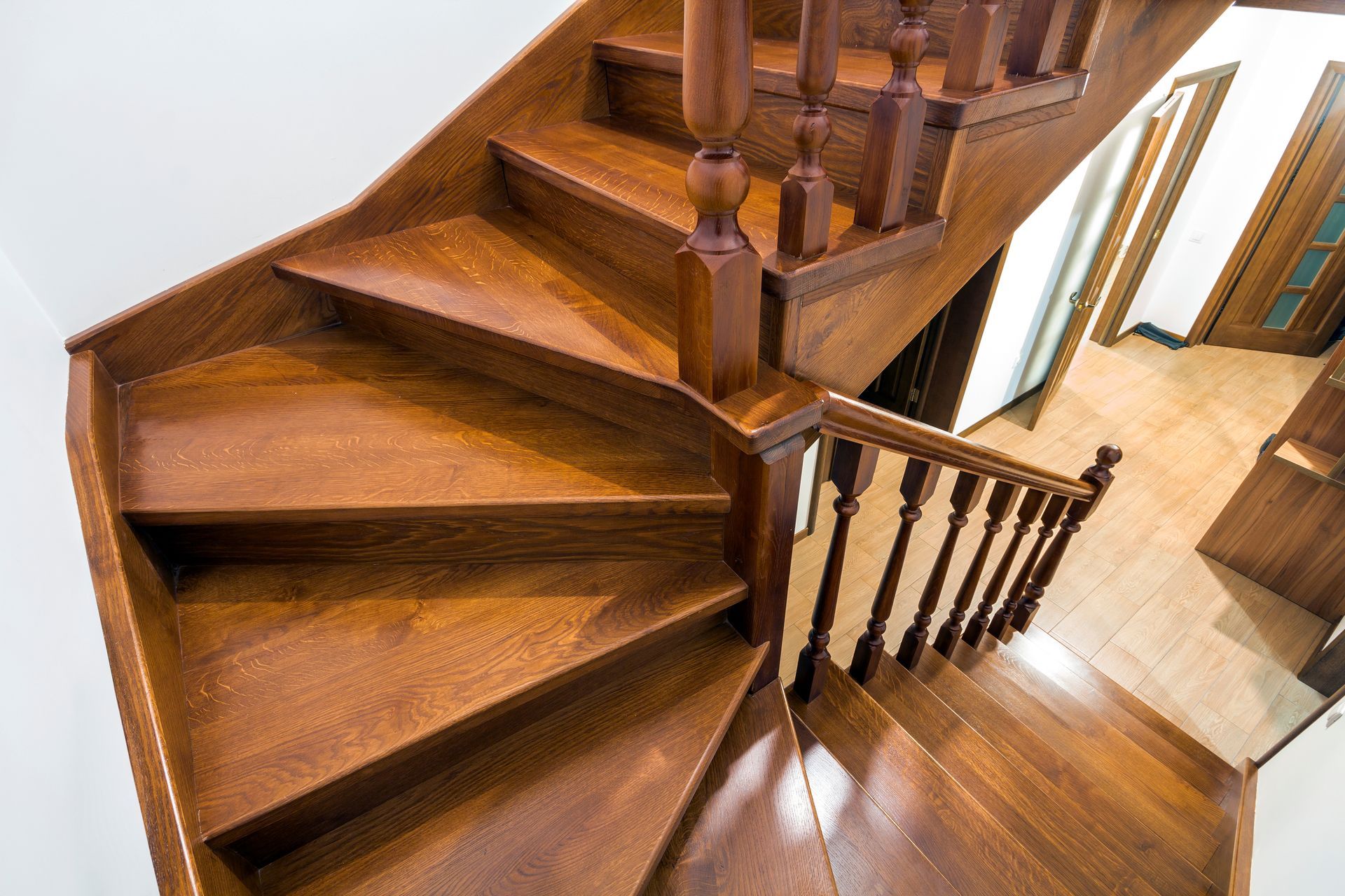 Wooden staircase with brown treads and handrail, leading upwards and curving.