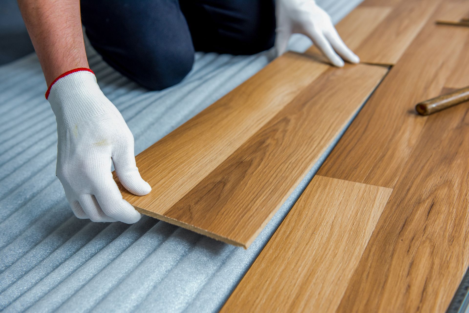 Hands in white gloves installing wood floor planks.