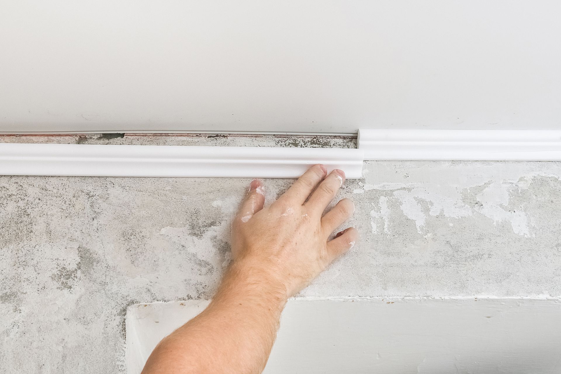 Hand placing white molding on a textured wall, near the ceiling.