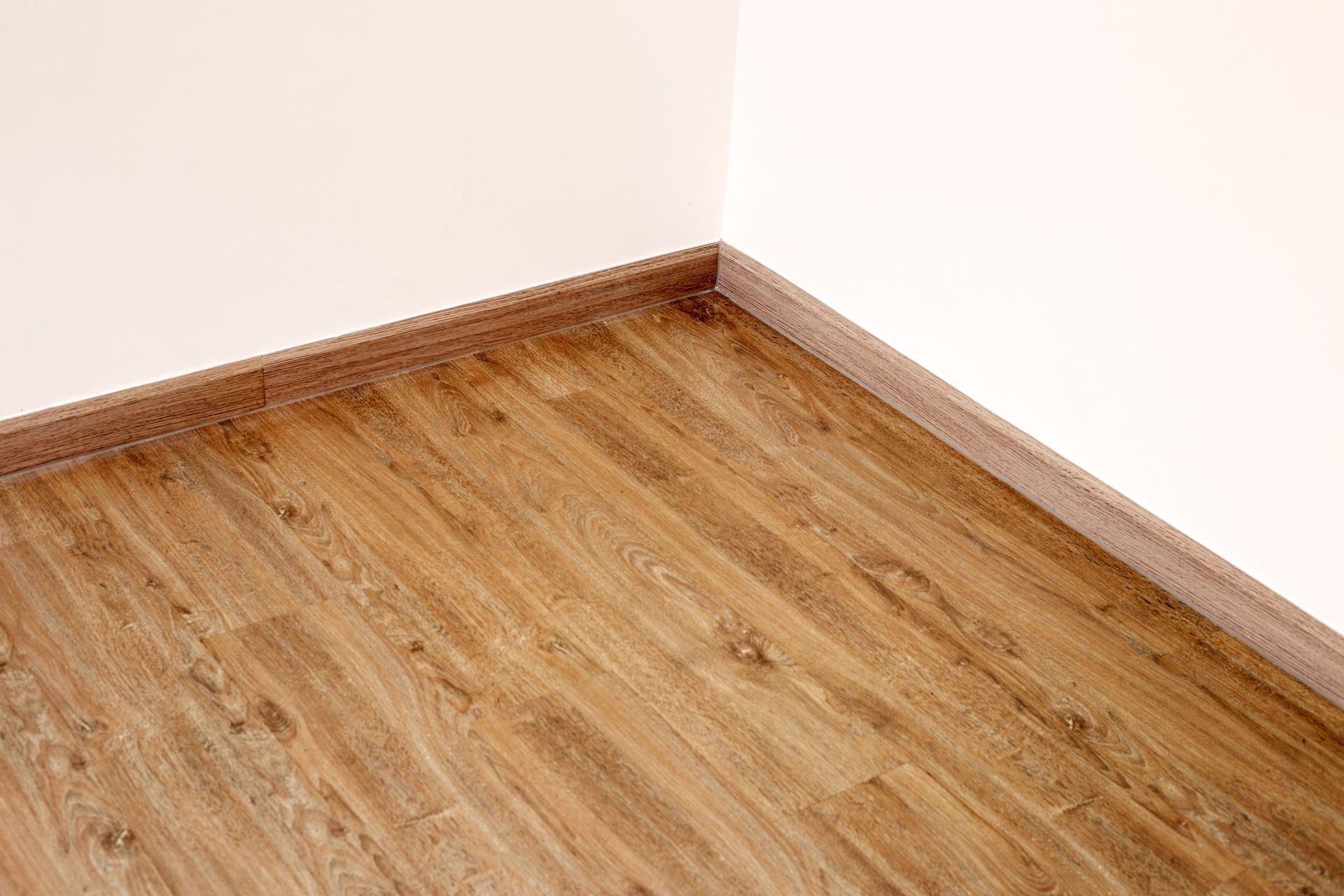 Corner of a room with light wood flooring, tan baseboards, and white walls.