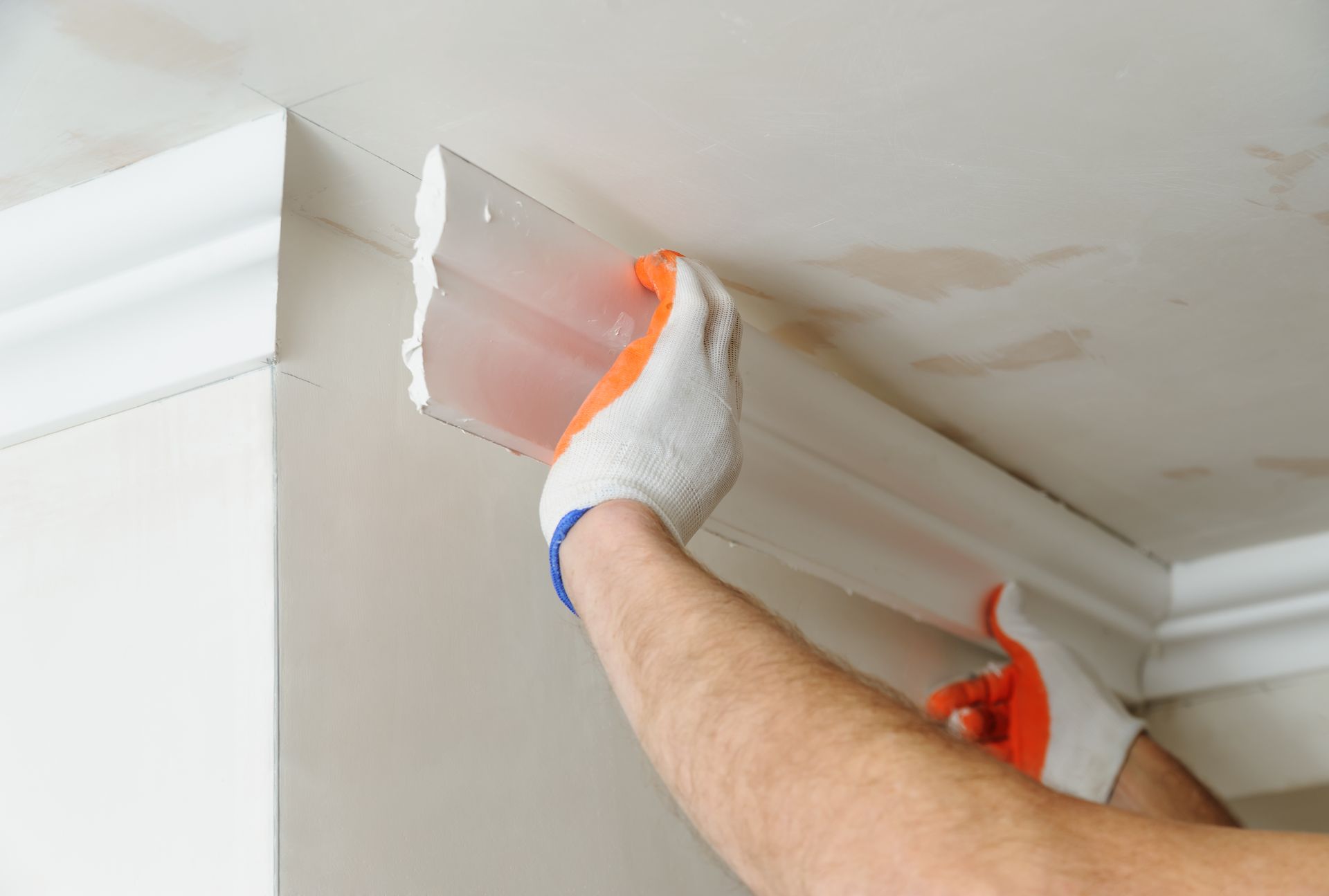 Person wearing gloves installing crown molding on a wall and ceiling.