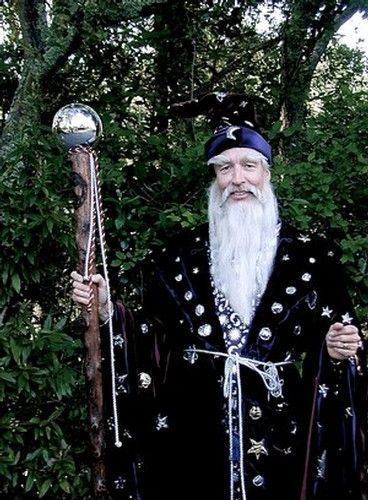 A person dressed as a wizard in a dark, star-patterned robe and hat, holding a wooden staff topped with a silver sphere.