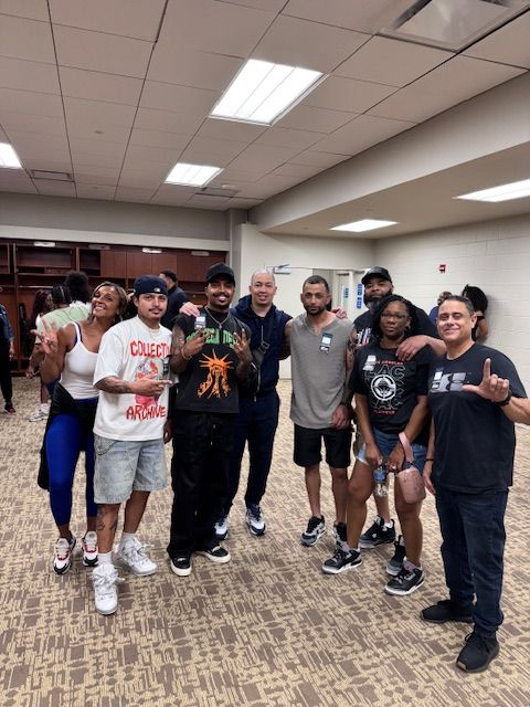 Group of people posing together indoors, some smiling. Well-lit room with patterned carpet and overhead lights.