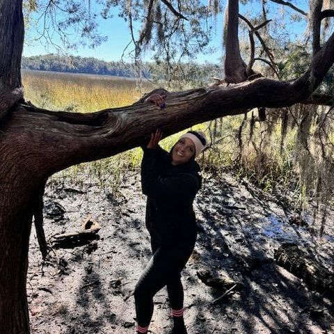 Woman hanging from tree branch near marsh.