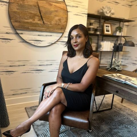 Woman in black dress sits in a chair, legs crossed, in a home office.