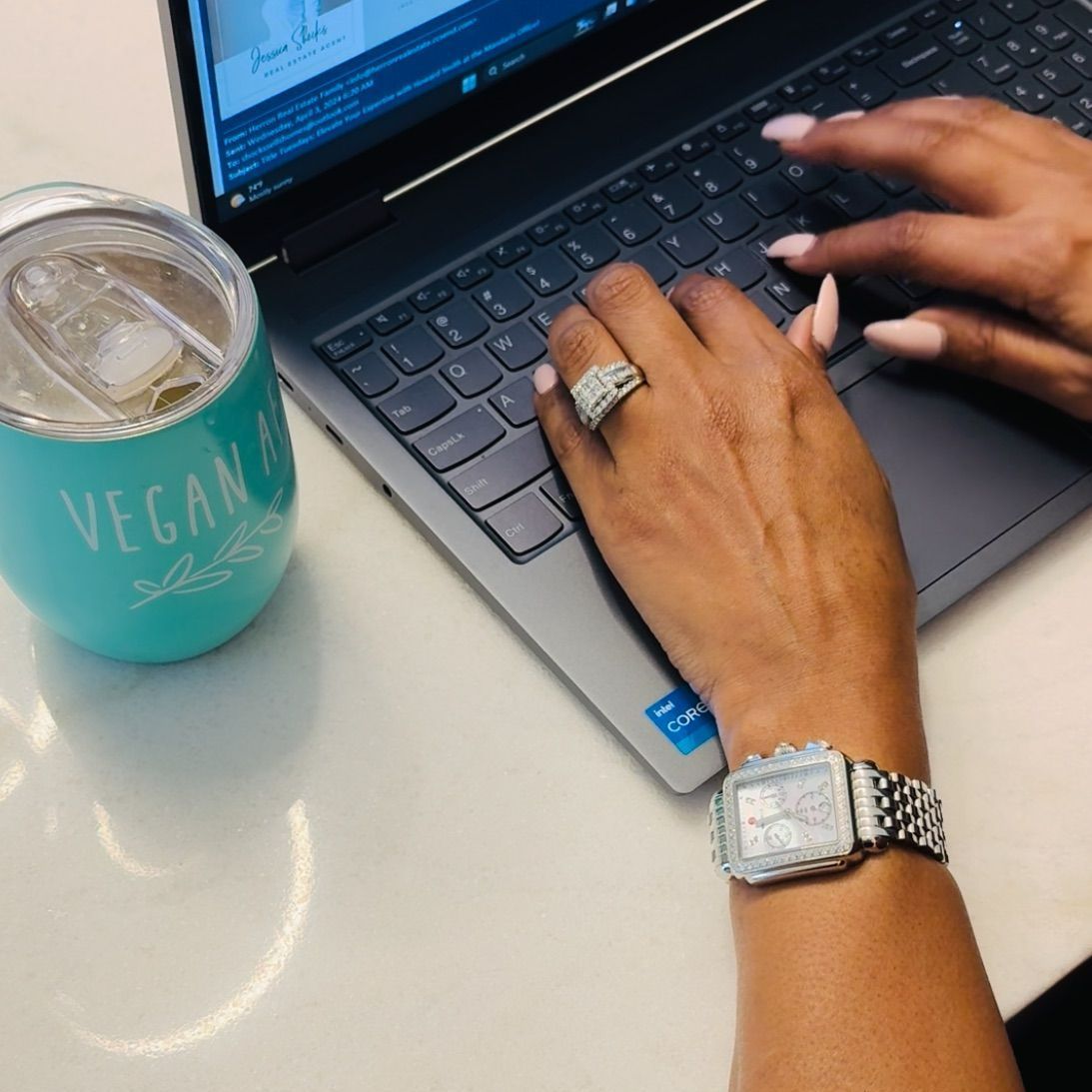 Person typing on a laptop with a watch, ring, and a teal 
