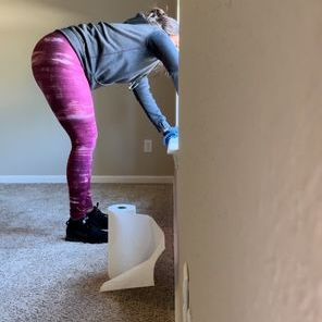 Person bends over to wipe a wall with paper towels, floor is carpeted.