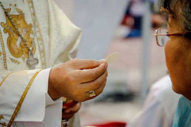 Priest offering communion wafer to a person at church service.