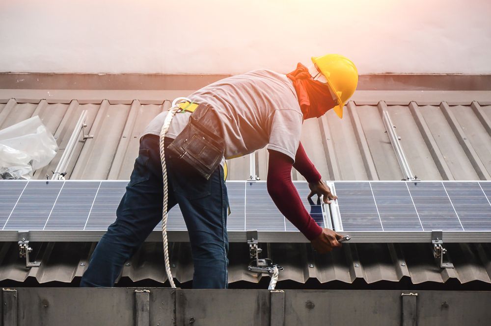 A Worker Installs Solar Panels on a Metal Roof — Macleay Energy Solutions In Kempsey, NSW