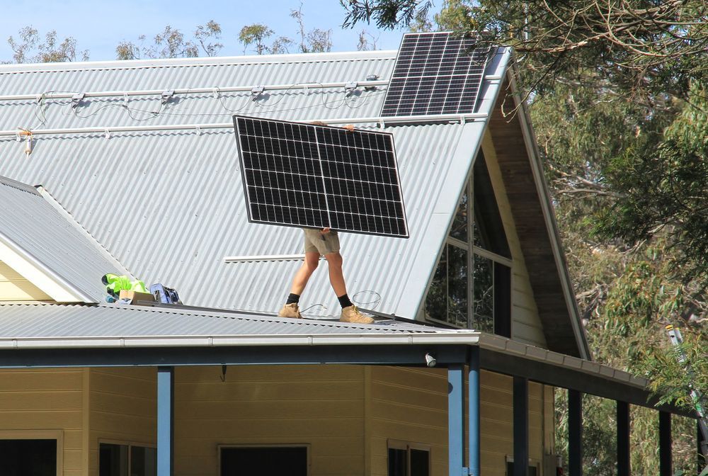 A Person Carrying a Large Black Solar Panel — Macleay Energy Solutions In Macksville, NSW