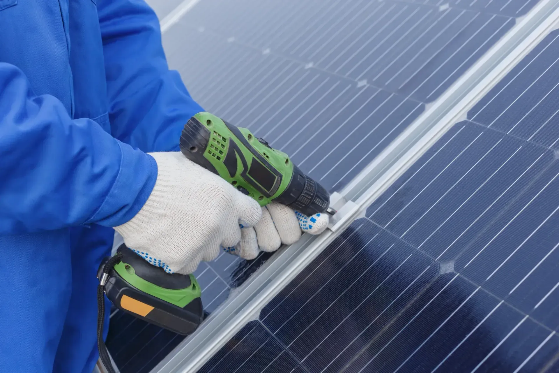 Worker in blue jacket using a power drill to install a solar panel on a rooftop — Macleay Energy Solutions In Kempsey, NSW